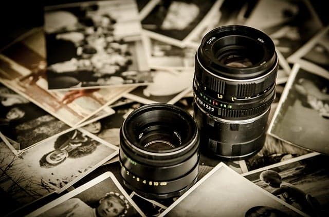 Two camera lenses resting on a pile of old photographic prints