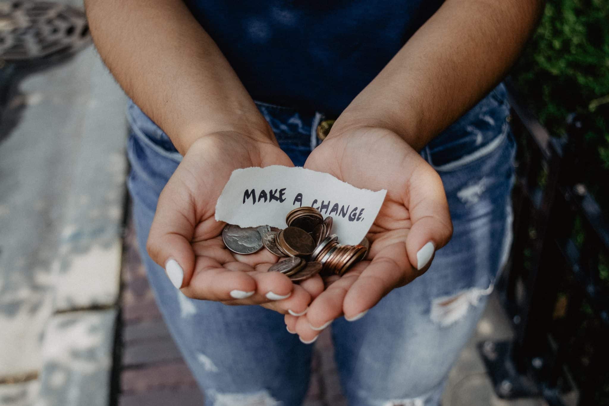 Cupped hands holding coins and a handwritten note reading make a change