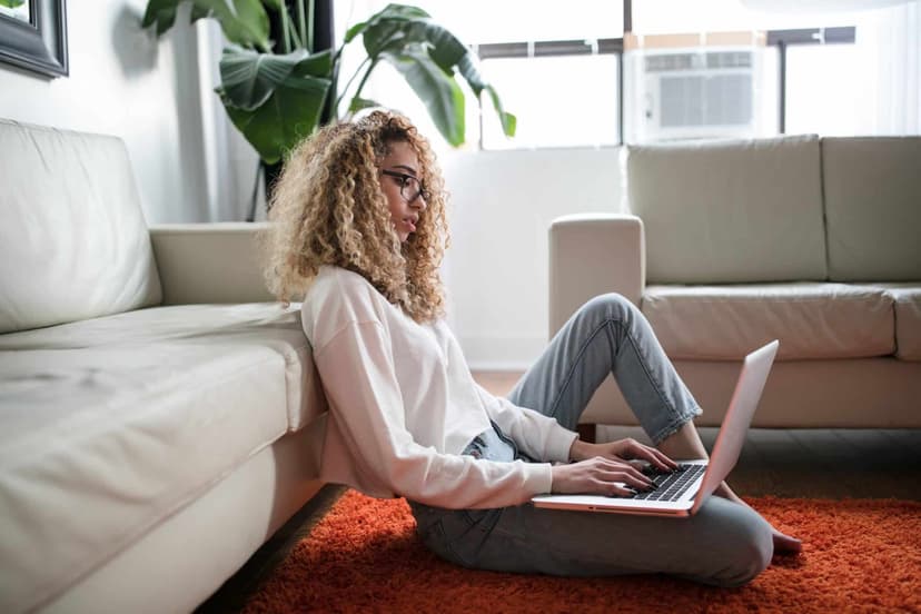 A person sitting on the floor by a sofa working on a laptop