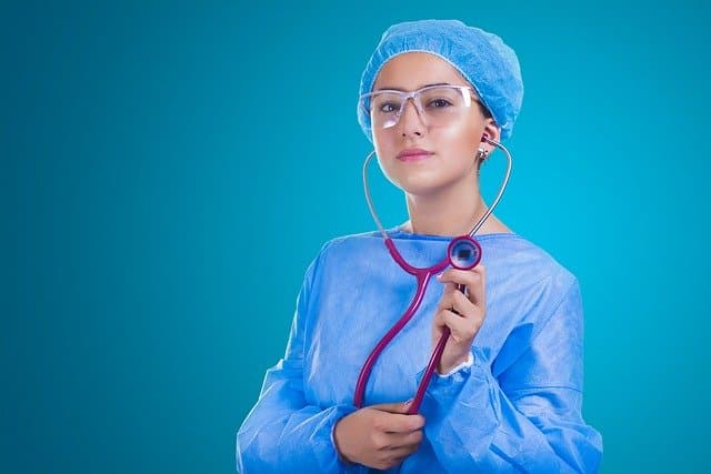 A person in medical scrubs holding a stethoscope against a blue background