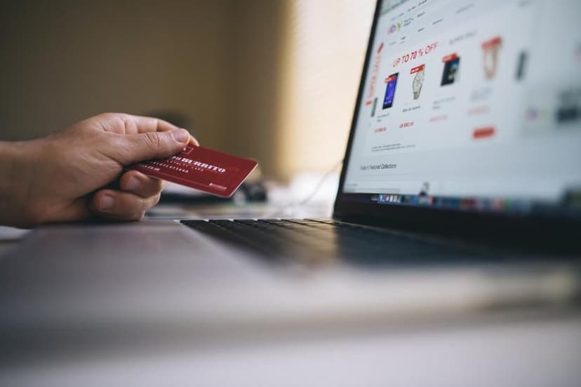 A hand holding a credit card in front of a laptop showing an online store