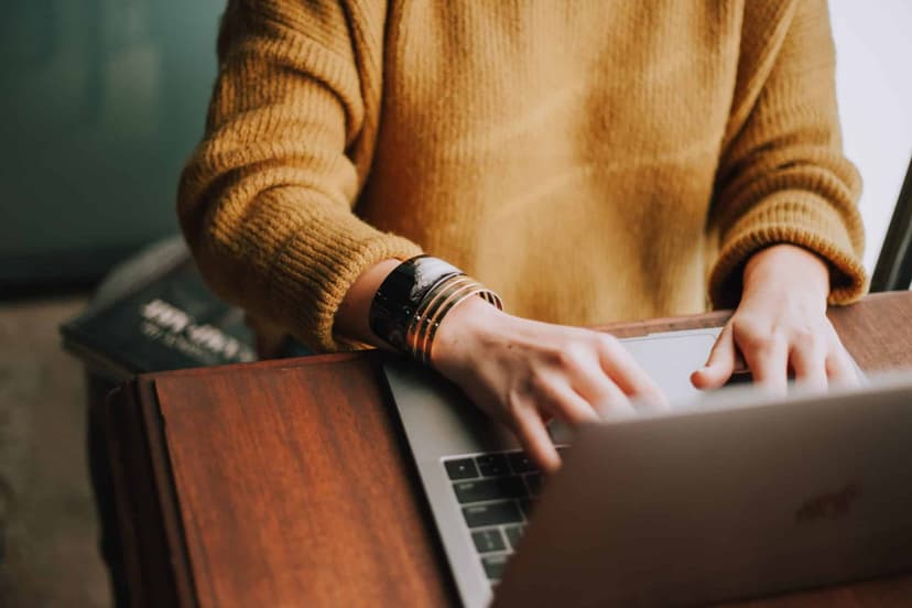A person in a knitted jumper typing on a laptop