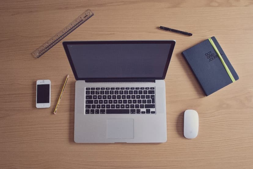 A laptop, phone, notebook and ruler arranged on a wooden desk