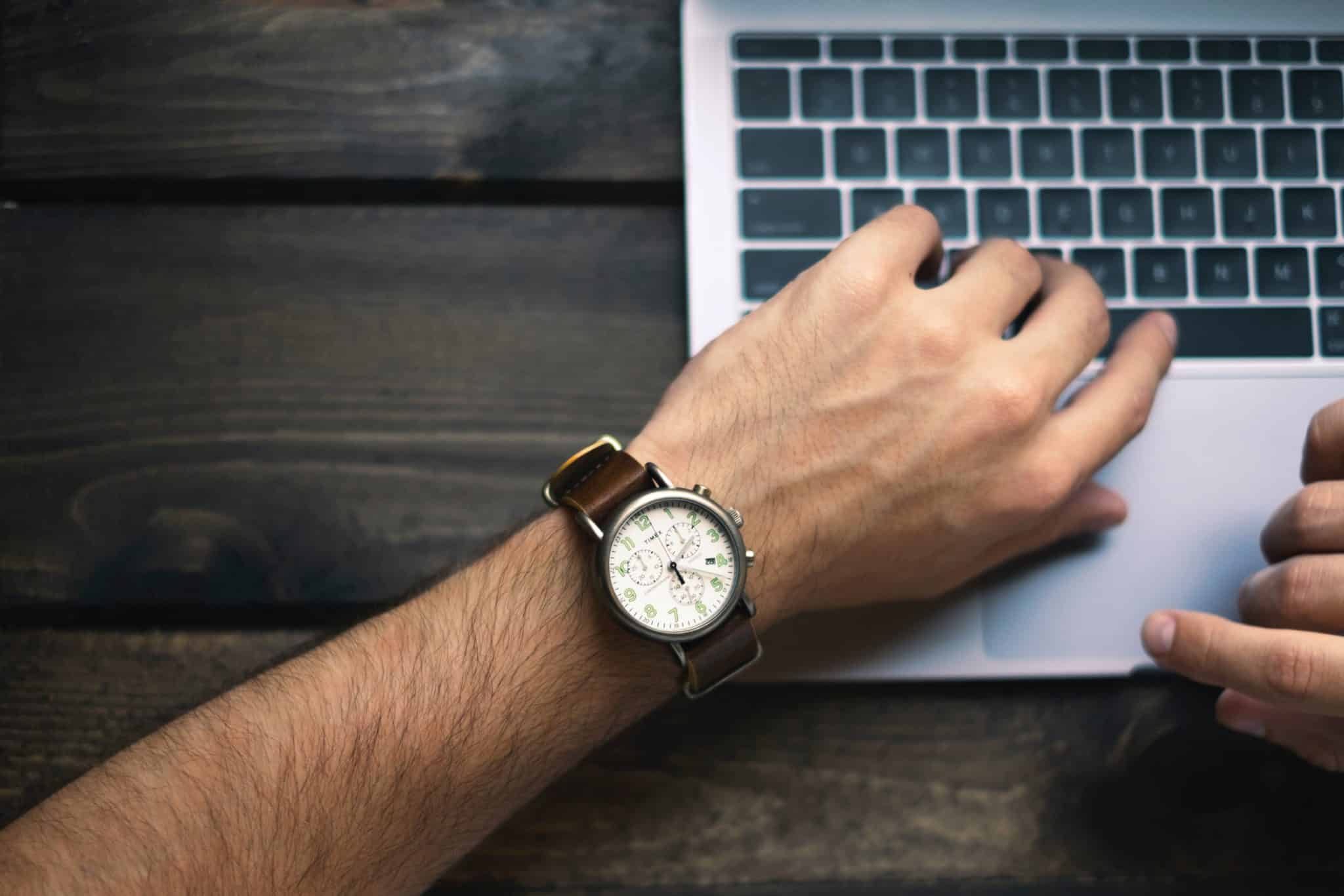 A wrist wearing a watch resting on a laptop keyboard