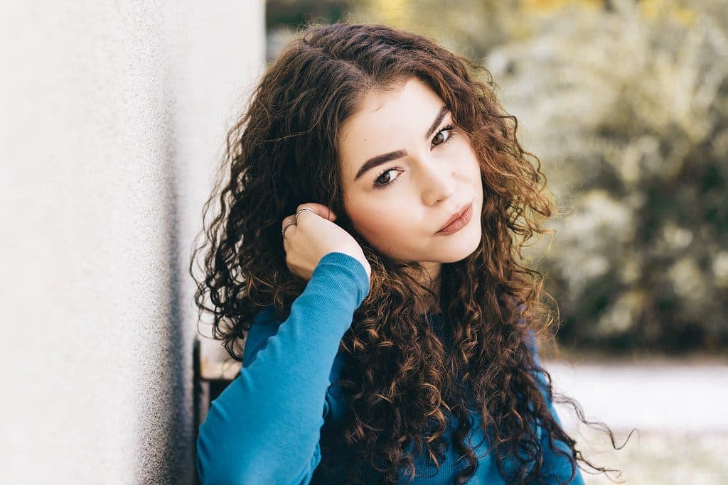 A portrait of a person posing outdoors against a pale wall