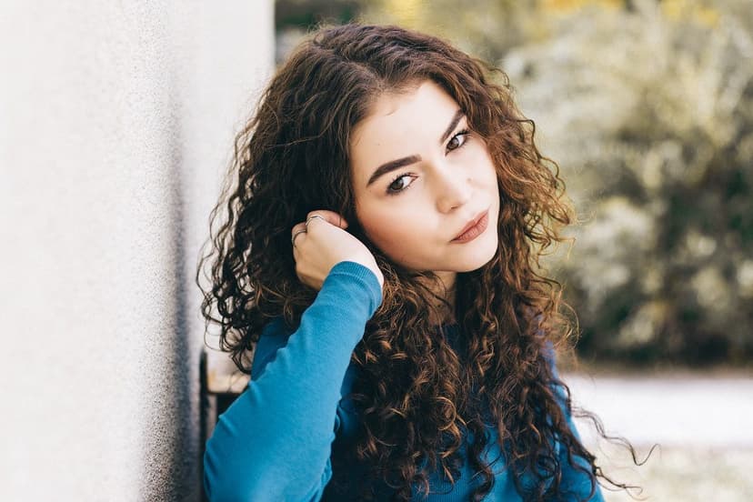 A portrait of a person posing outdoors against a pale wall