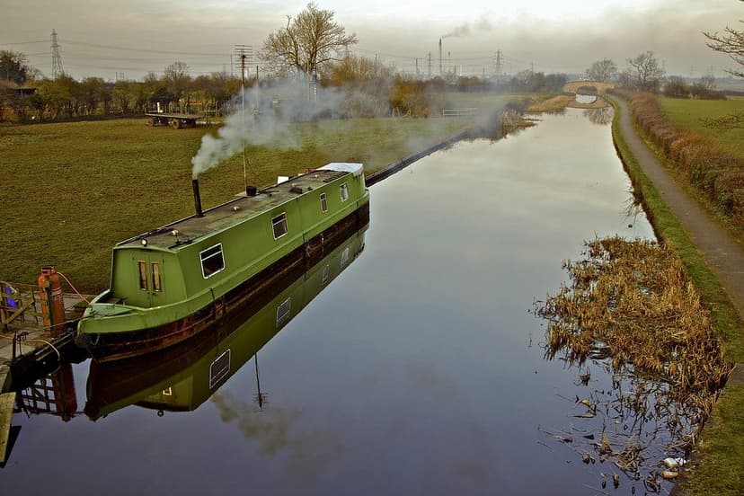 A narrowboat cruising along a canal through open countryside